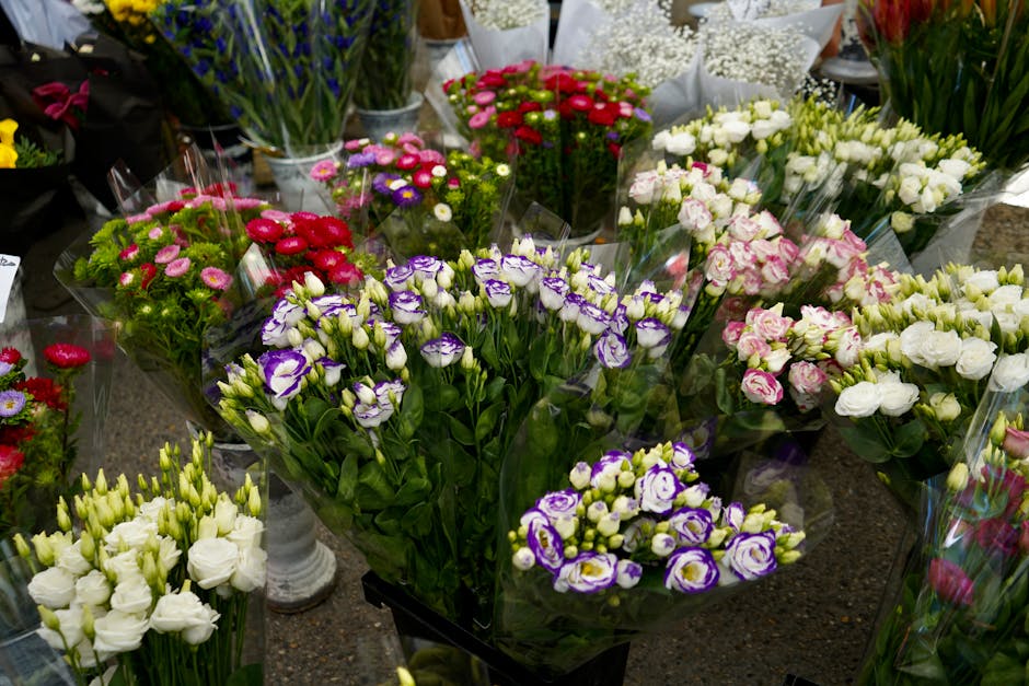 A vibrant display of fresh floral arrangements consisting of various flowers such as purple and white lisianthus, pink and white roses, red chrysanthemums, and white lisianthus, all wrapped in transpa