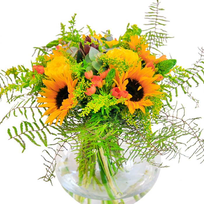The first impression this bouquet gives is pure, golden exuberance-sunflowers and yellow roses beaming together as if they've gathered all the sunlight streaming through Grove Park's leafy lanes. The sunflowers, generous and open, anchor the design with their earthy brown centers and halos of yellow-orange petals, projecting warmth into any space. Woven artfully amongst them are garden roses, each bloom tightly formed like a miniature sunrise, their petals rich and luxurious to the touch. Sprays of bright red Hypericum berries nestle within the greenery, a sparkling contrast to the mellow palette, reminiscent of autumn leaves scattered across the grass in Chiswick's green commons. Fern fronds and airy goldenrod spill outwards in soft, natural arcs, adding movement and life, while eucalyptus leaves introduce a silvery, contemporary twist. The arrangement rests serenely within a crystal-clear fishbowl vase, water glinting beneath the lush stems, grounding the profusion above with a sense of clarity and poise. Flecks of light play over the blooms, and if you lean in close, you might imagine the subtle mix of sweet rose, green freshness, and sun-warmed petal. This bouquet, crafted by the experienced hands at Grove Park Flowers, is perfect for celebrating milestones-birthdays, anniversaries, or any occasion that calls for brightness and cheer. Its bold character and gentle textures make it not just a gift, but a statement of happiness, local pride, and artistic skill.