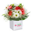 Bathed in generous natural light, this exuberant bouquet stands nestled in a modern white gift bag, ready to spread joy throughout Grove Park. The vivid coral and soft peach shades of the carnations evoke sunrise over verdant local gardens, their plentiful ruffled petals offering a textured, tactile feast. Bright white daisies with sparkling yellow-green centers emerge between the carnations, their cheerful countenances shining like familiar faces on a sunny walk down Grove Park Road. Wisps of white baby's breath thread delicately throughout, casting an ethereal softness that lightens the whole presentation. Lower in the arrangement, secretive hints of purple-blushed buds appear, suggesting future blooms and hinting at the passage of seasons-a nod to the ever-changing landscape of west London. Deep emerald foliage and broad leaves embrace the bouquet, their glossy surfaces catching and reflecting the light to offer a lush backdrop to the star attractions. The arrangement, perfectly rounded and thoughtfully composed, radiates freshness and sincerity. Its placement in a stylish white bag begs to be gifted, marking occasions both grand and understated-an anniversary in Chiswick, a birthday in Grove Park itself, or a spontaneous gesture to brighten a neighbour's week. It's a vivid illustration of expert local floristry and the heartfelt creativity that Grove Park Flowers brings to every carefully prepared bouquet.